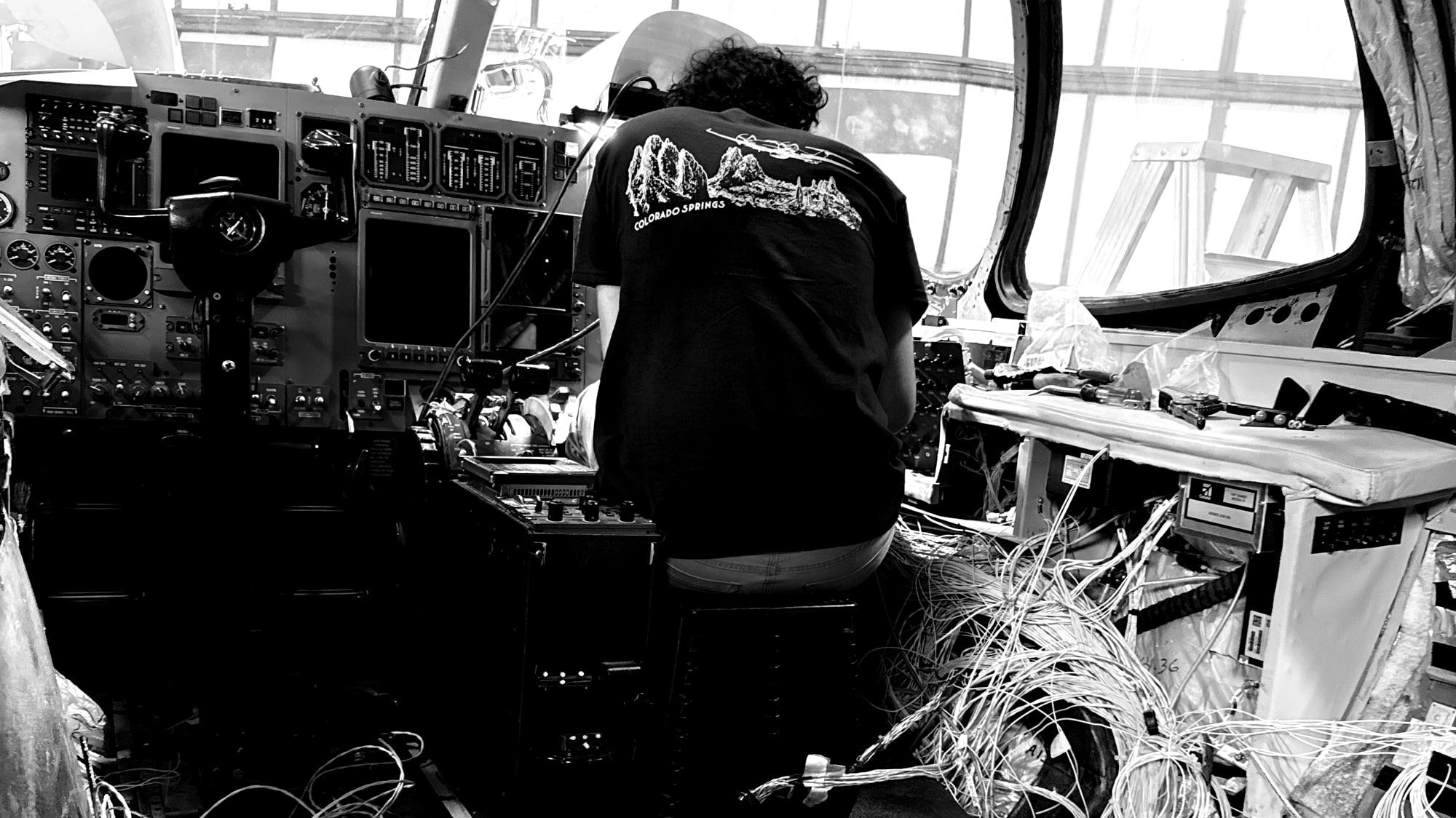 Technician seated in a stripped cockpit wiring a full panel at Colorado Springs